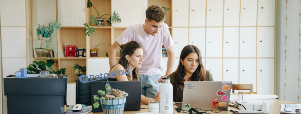 En la imagen se ve una escena de oficina y un grupo de personas que trabajan en la empresa IT Patagonia, trabajando en una computadora portátil.