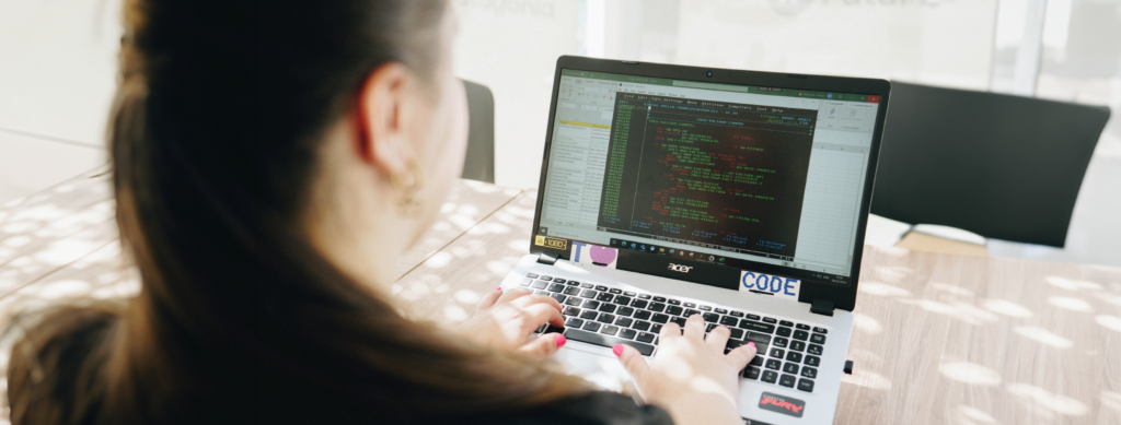 En la imagen se ve a una mujer sentada de espaldas, escribiendo un programa en lenguaje COBOL. 