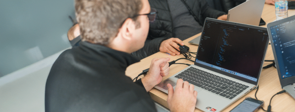 En la imagen se ve una persona joven de espalda trabajando en una computadora portátil. En la pantalla de la computadora se visualiza lenguajes COBOL.