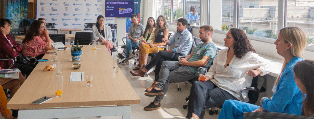 En la imagen se ve a un grupo de personas en un entorno de oficina, compartiendo ideas en un ambiente distendido. Las personas están sentadas en forma de ronda.