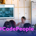 En la imagen se ve a un grupo de personas jóvenes reunidas en una formación sobre tecnología. Una mujer joven está compartiendo información a una audiencia.