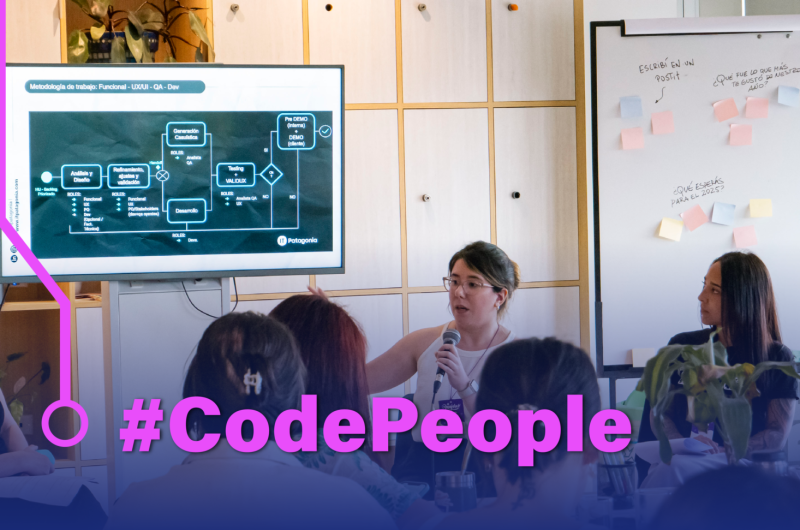 En la imagen se ve a un grupo de personas jóvenes reunidas en una formación sobre tecnología. Una mujer joven está compartiendo información a una audiencia.